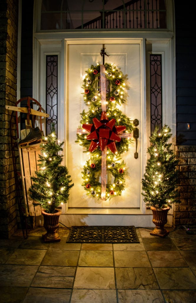 trio of wreaths flanked by two planters with string lights to create outdoor lighted Christmas decorations.